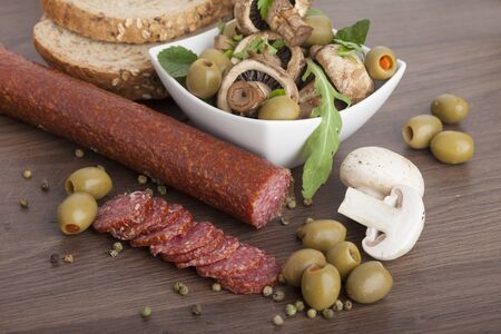 Salami sausage on a wooden table with mushrooms and olivesの写真素材