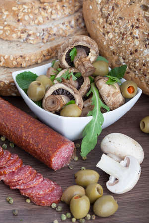 Salami sausage on a wooden table with mushrooms and olivesの写真素材