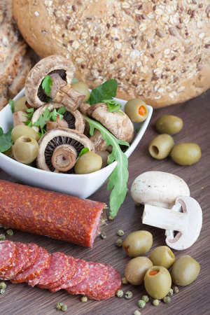 Salami sausage on a wooden table with mushrooms and olivesの写真素材