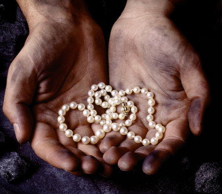 White pearl necklace in the hands of a coalminer with black coal aroundの写真素材
