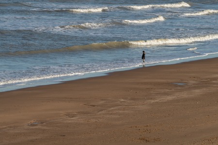 Lone boy standing on the beach with his feet in the seaの写真素材