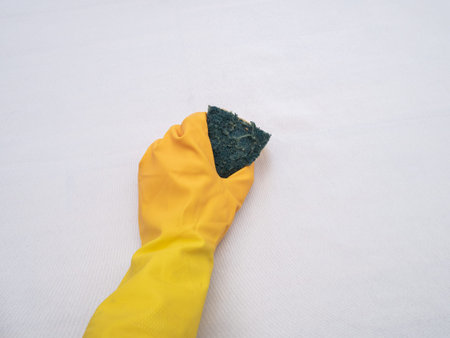 Hands wearing bright yellow rubber gloves on a white cloth background