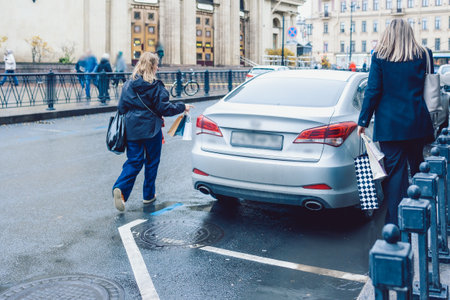 Two women hail taxi after leaving store with shopping bagsの写真素材