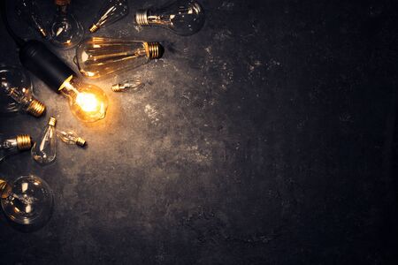 Vintage old light bulb glowing yellow on rough dark background surrounded by burnt out bulbs. Idea, creativity concept.の写真素材