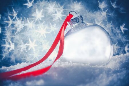 Clear Christmas ornament in snow surrounded by a bokeh of glittering lights in the shape of snowflakes.の写真素材