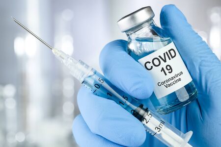 Healthcare cure concept with a hand in blue medical gloves holding Coronavirus, Covid 19 virus, vaccine vialの写真素材