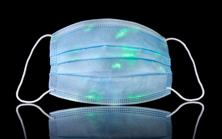 Contaminated medical face mask with glowing green spots representing germs, bacteria, or corona...