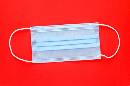 Personal protective equipment, PPE. Single disposable medical face mask on red background.
