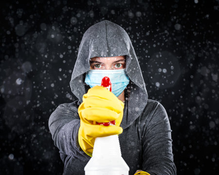 Woman wearing medical mask and cleaning gloves spraying a mist of disinfectant. Serious about...