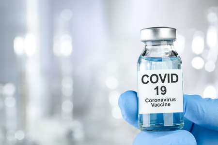 Healthcare cure concept with a hand in blue medical gloves holding Coronavirus, Covid 19 virus, vaccine vialの写真素材