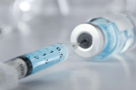 Healthcare and pharmaceutical drugs concept with syringe needle piercing the vaccine vial with blue liquid.の写真素材
