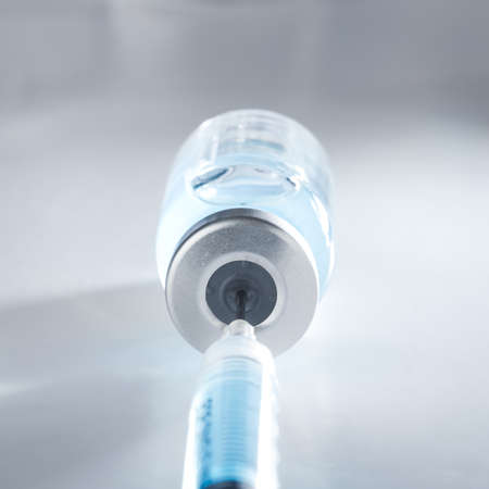 Healthcare and pharmaceutical drugs concept with syringe needle piercing the vaccine vial with blue liquid.の写真素材