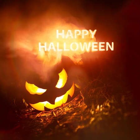 Happy Halloween text glowing in red and yellow smoke at night above a creepy pumpkin Jack o Lanternの写真素材