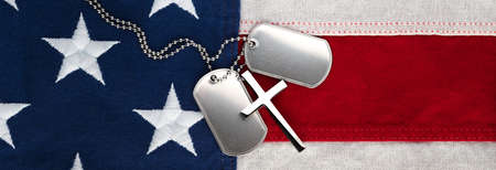 US military soldier's dog tags, rough and worn with blank space for text, and Christian cross necklace on American flag. Memorial Day or Veterans Day concept.の写真素材