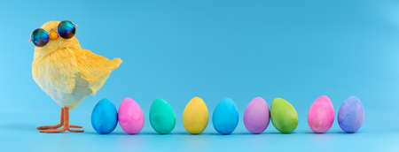 Easter decoration of a yellow chick wearing silly sunglasses with a row of colorful painted Easter eggs.の写真素材