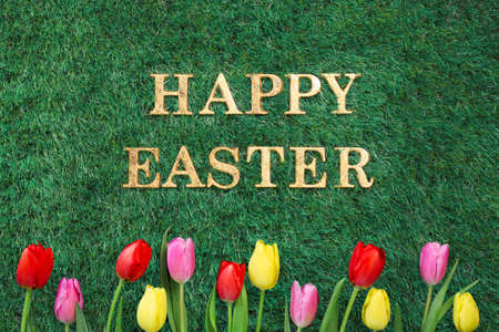 Happy Easter text on green grass with colorful tulips.の写真素材
