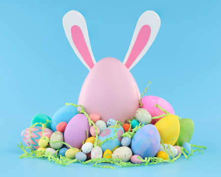 Large pink Easter egg with bunny ears surrounded by a pile of colorful Easter eggs and candy.の写真素材