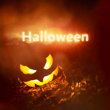 Halloween text glowing in red and yellow smoke at night above a creepy pumpkin Jack o Lanternの写真素材