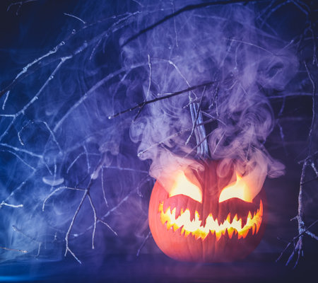 Spooky Halloween jack o lantern pumpkin with carved scary face glowing and billowing smoke in the night.の写真素材