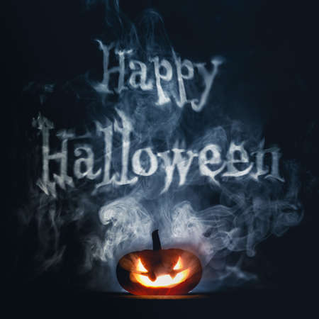 Spooky Halloween jack o lantern pumpkin with carved scary grinning face glowing in smoke on Halloween night, with Happy Halloween text.の写真素材