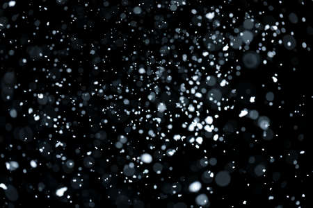 Blurry bokeh of falling white snow on black backgroundの写真素材