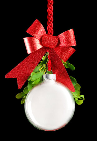 White Christmas ornament hanging by red ribbon rope with the bauble surrounded with green mistletoe.の写真素材