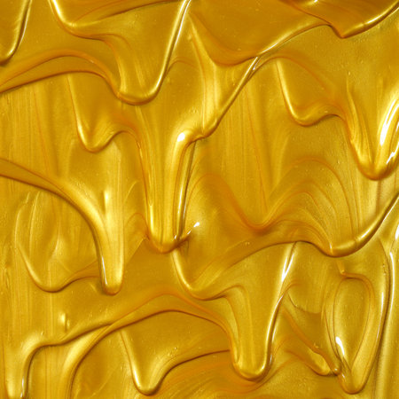 Glittering shiny metallic gold paint flowing and dripping downward making a golden background.の写真素材