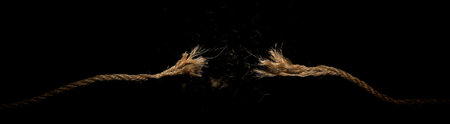 Long dirty rope, frayed at both ends and snapped in two. Concept of dangerous stress or stressful situation like divorce separation, deadlines, failure, or tension.の写真素材