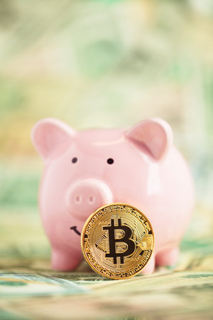 Golden bitcoin on piles of money leaning on pink piggy bank. Wealth, savings, digital, virtual, currency, and cryptocurrency concept.の写真素材