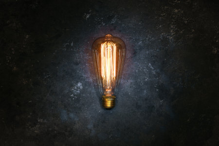 Vintage old light bulb glowing yellow on rough dark background. Idea, creativity concept.の写真素材