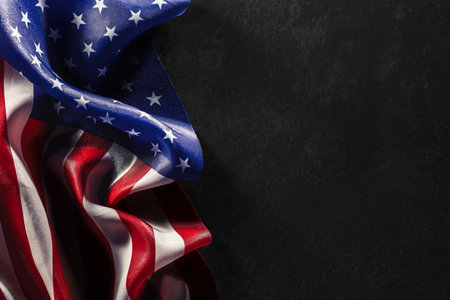 Ruffled USA flag on dark black background with copyspace for text. US American flag background for Memorial Day, Veteran's Day, 4th of July, or other patriotic event.の写真素材