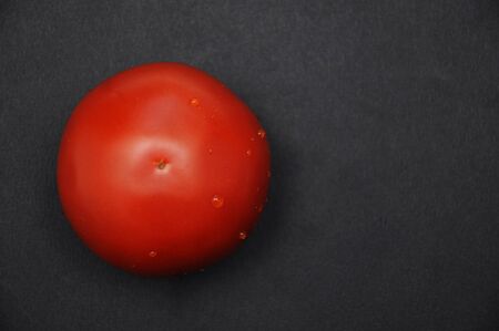 Red fresh tomato on a black background with water dropsの写真素材
