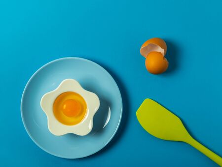 Raw eggs on a solid blue color background with various kitchen utensils, plates and bowlsの写真素材