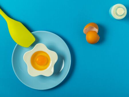Raw eggs on a solid blue color background with various kitchen utensils, plates and bowlsの写真素材