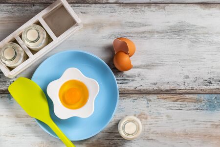 Top view of a rustic kitchen table with raw egg in a flower shaped bowl with milk bottles and kitchen utensils. Bottle, herbs.の写真素材