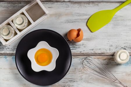 Top view of a rustic kitchen table with raw egg in a flower shaped bowl with milk bottles and kitchen utensils. Bottle, herbs.の写真素材