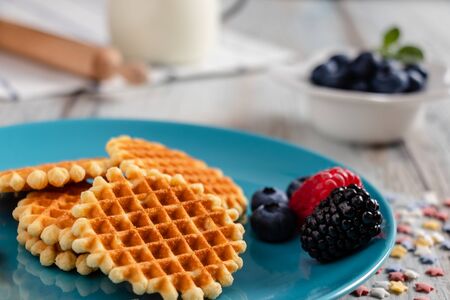 Traditional Belgian waffles with fresh fruit and milk. Rustic kitchen table. Various plates and kitchen utensils.の写真素材