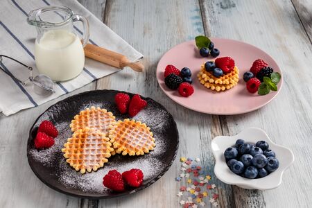 Traditional Belgian waffles with fresh fruit and milk. Rustic kitchen table. Various plates and kitchen utensils.の写真素材