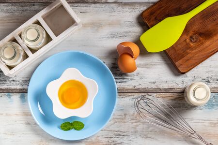 Top view of a rustic kitchen table with raw egg in a flower shaped bowl with milk bottles and kitchen utensils. Bottle, herbs.の写真素材