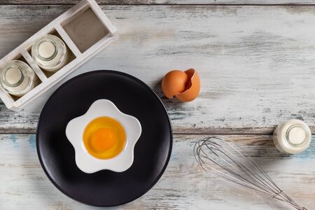 Top view of a rustic kitchen table with raw egg in a flower shaped bowl with milk bottles and kitchen utensils. Bottle, herbs.の写真素材