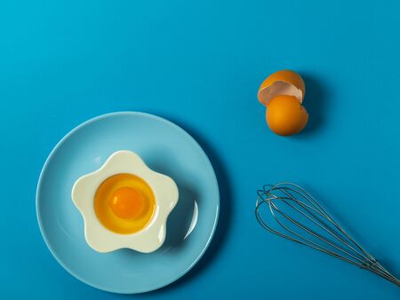 Raw eggs on a solid blue color background with various kitchen utensils, plates and bowlsの写真素材