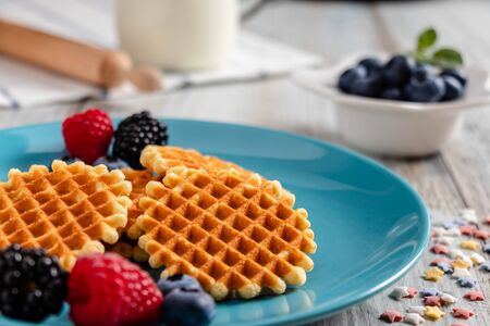 Traditional Belgian waffles with fresh fruit and milk. Rustic kitchen table. Various plates and kitchen utensils.の写真素材