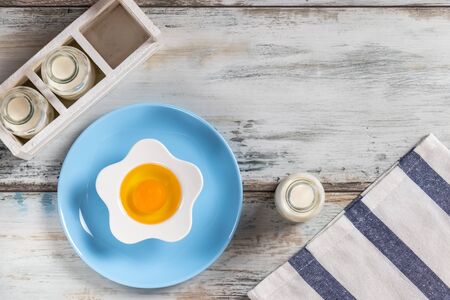 Top view of a rustic kitchen table with raw egg in a flower shaped bowl with milk bottles and kitchen utensils. Bottle, herbs.の写真素材