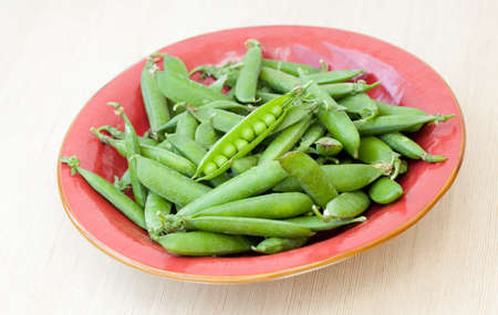 Fresh peas pods in a red plate on wooden backgroundの写真素材