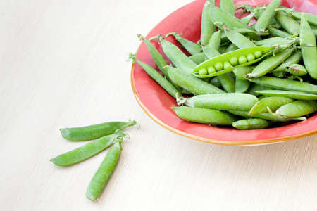 Closeup on a red plate of peeled fresh green peasの写真素材