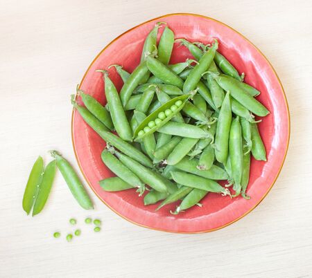 Closeup on a red plate of peeled fresh green peasの写真素材