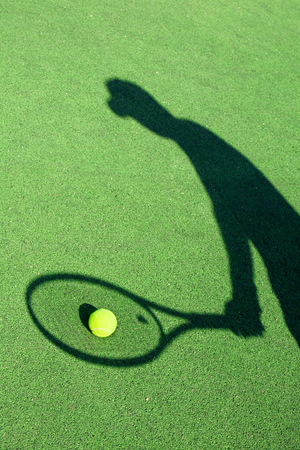 in action on a tennis court (conceptual image with a tennis ball lying on the court and the shadow of the player positioned in a way he seems to be playing it)の写真素材