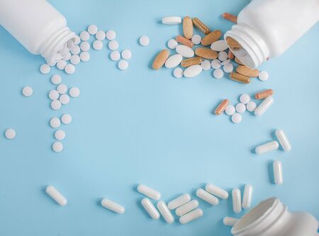 Tablets are scattered from three jars. Frame of different pills on a blue background. Flat lay with space for text.の写真素材