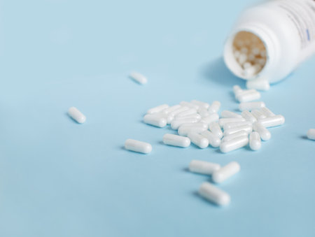 Medical capsules spilled out from white plastic bottle isolated on blue background.の写真素材