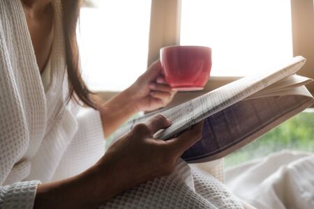 Beautiful female sitting on the bed and reading a book. Morning with a book. Relaxing concept. Retro filter effect,soft focus,selective focus.の写真素材